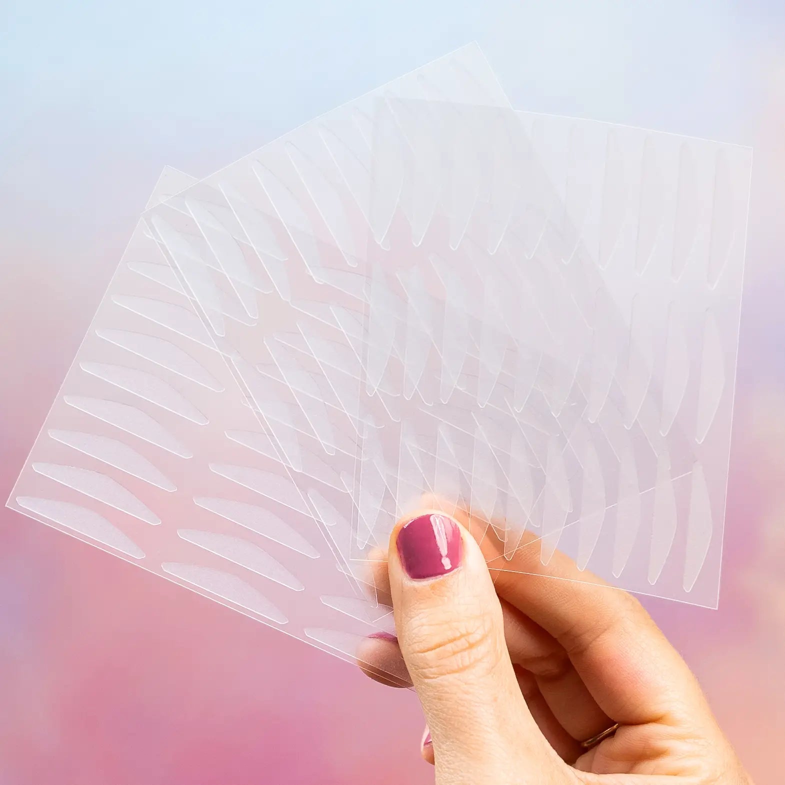 Original transparent GLARISE eyelid strip sheets held against a blush background